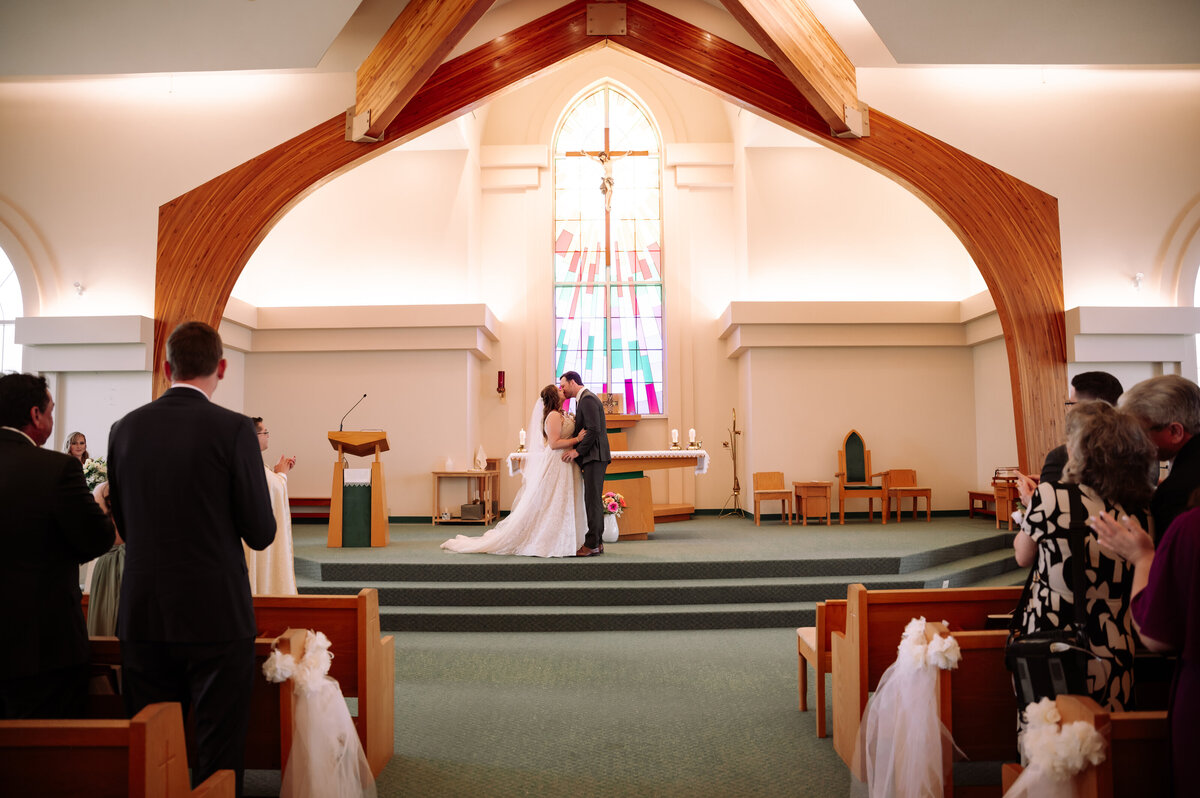 bride and groom share first kiss in Catholic Church, during wedding ceremony in Edmonton, Alberta
