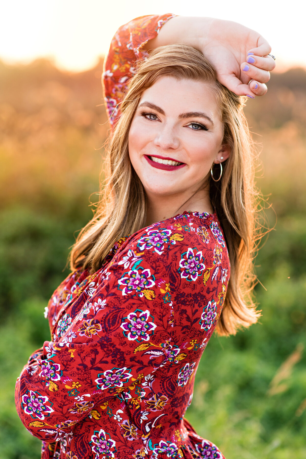 Mechanicsville high school senior girl wearing a red floral shirt poses in a field at sunset.