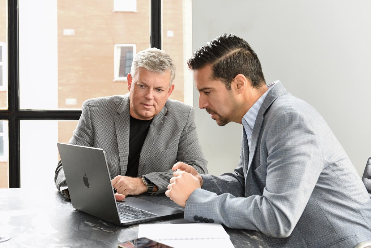 Corporate headshots featuring two professionals reviewing project plans on a laptop.