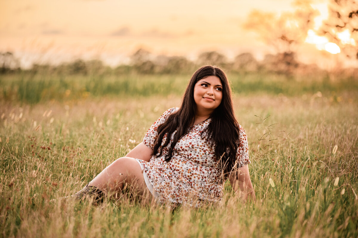 A senior at Chavez High School sits in a field and looks over her shoulder with a golden sunset in the sky.