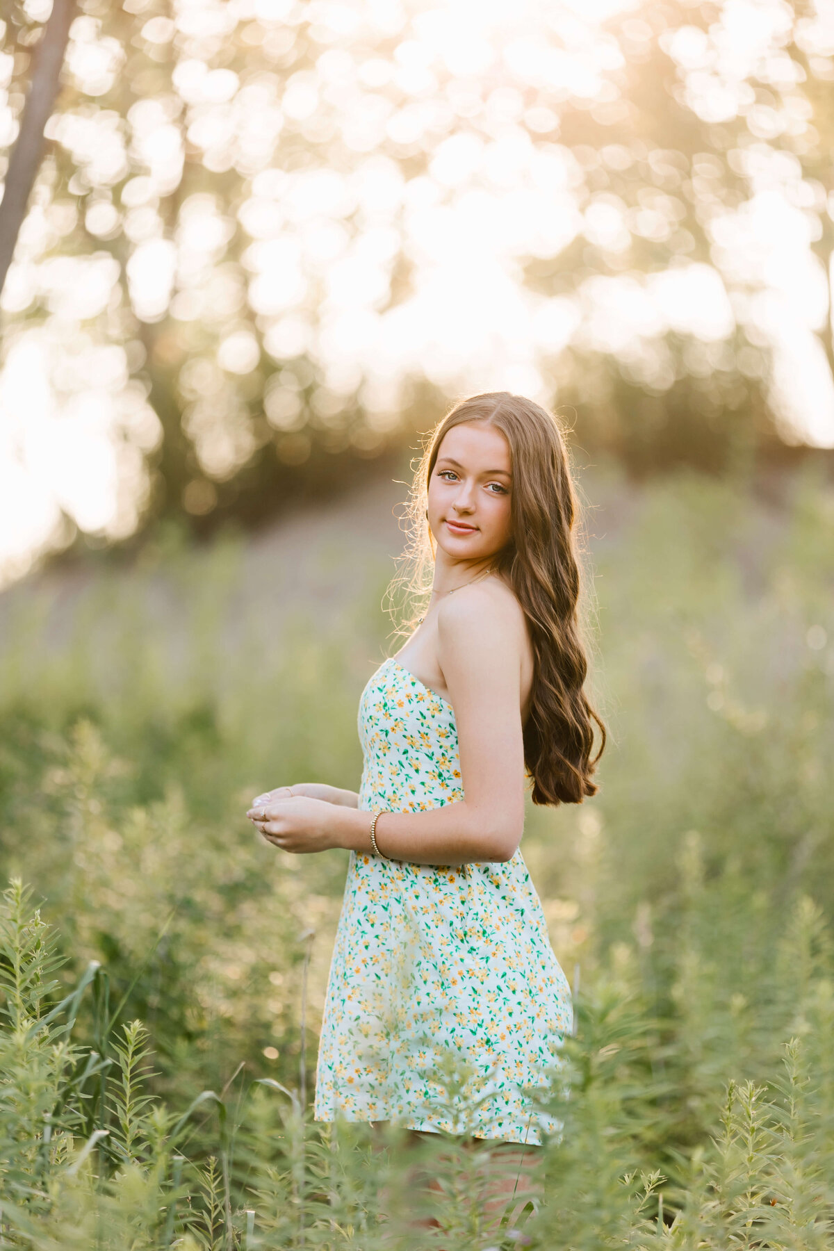 Senior portrait of a girl standing with the sun coming through the trees in the background