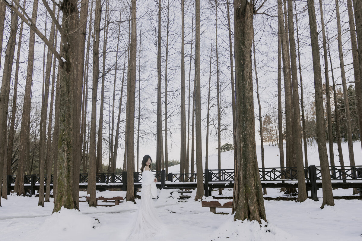 the bride wears her white long dress in a snowy forest in damyang south korea
