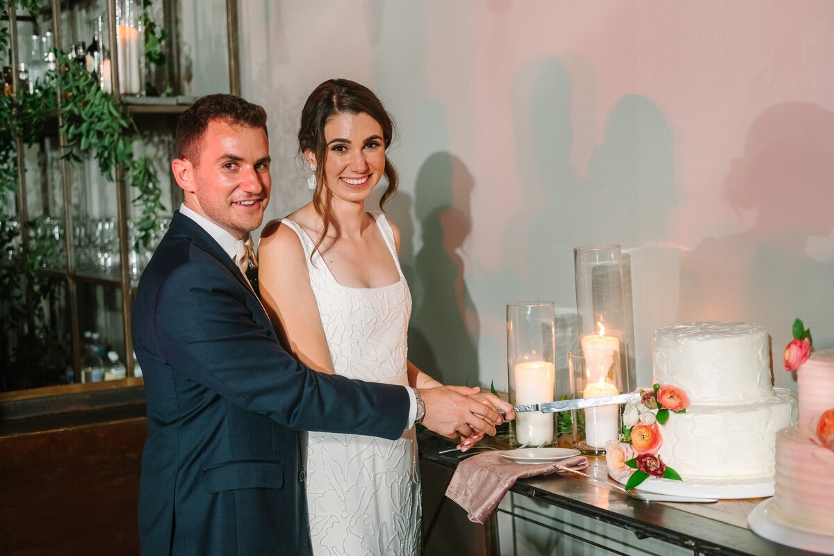Bride and groom cut their white wedding cake with peach flowers.