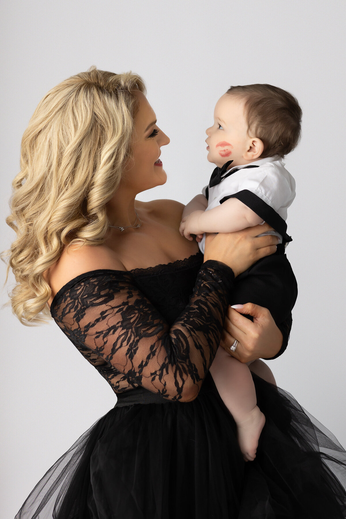 Milestone photo by a Dallas milestone photographer shows a mother in a lace gown holding her baby boy, who has a red lipstick kiss on his cheek.