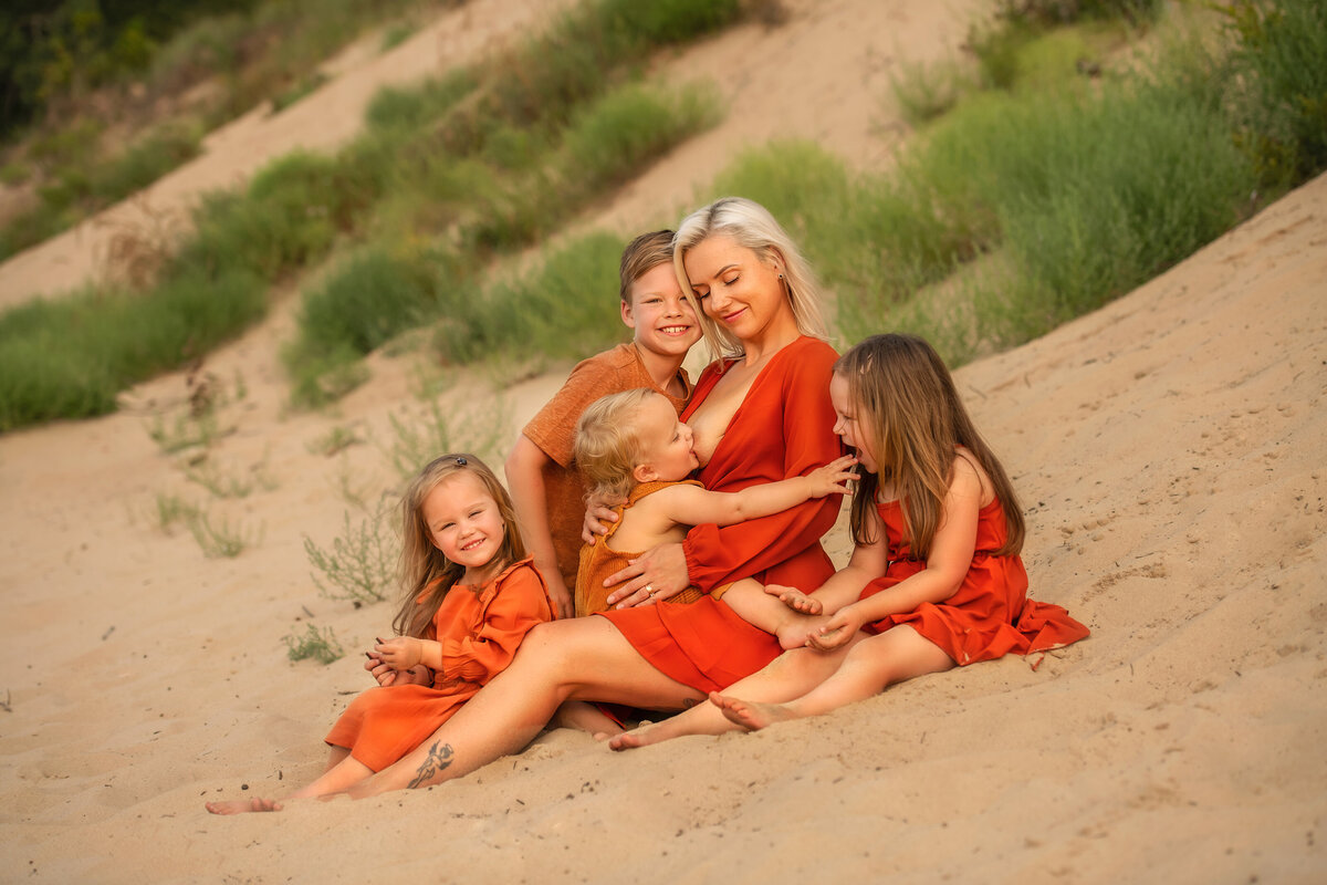 fours kids and their mother with matching orange outfits sitting on the sand at the beach.