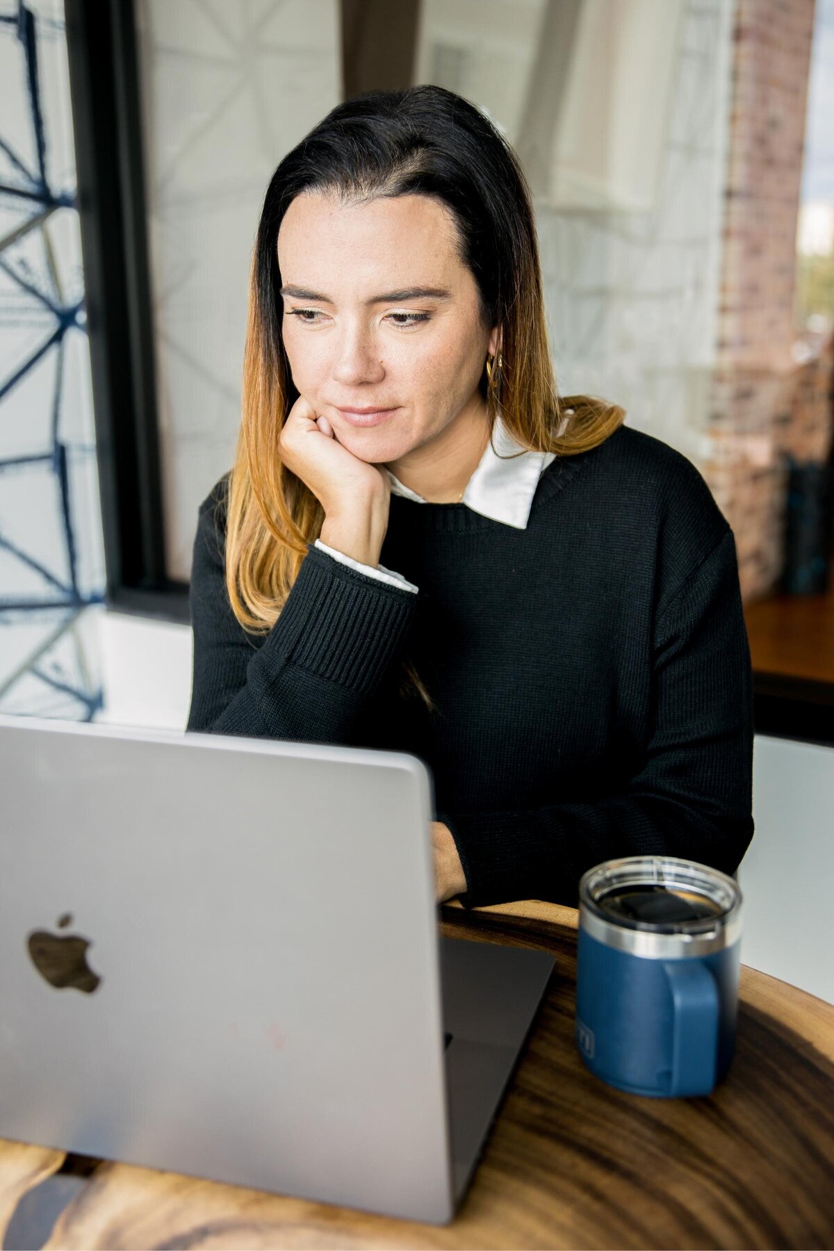 Carolina sitting with her hands on her chin while working on a laptop ideal for content on focused work, productivity, Perfect for brand photoshoots
