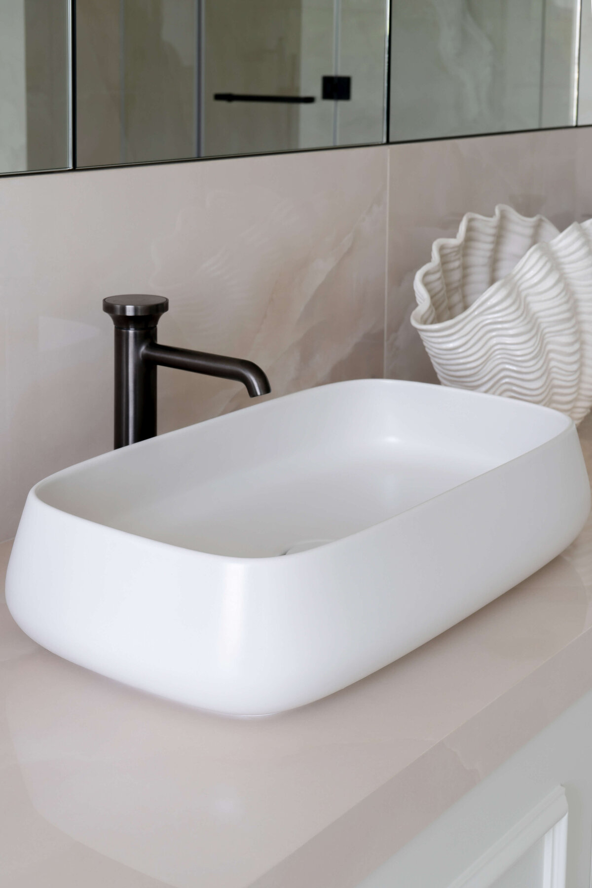 Close-up detail of a sink in the primary bathroom. The room is airy and light. The sink hardware is a stark black and contrasts the white bowl.