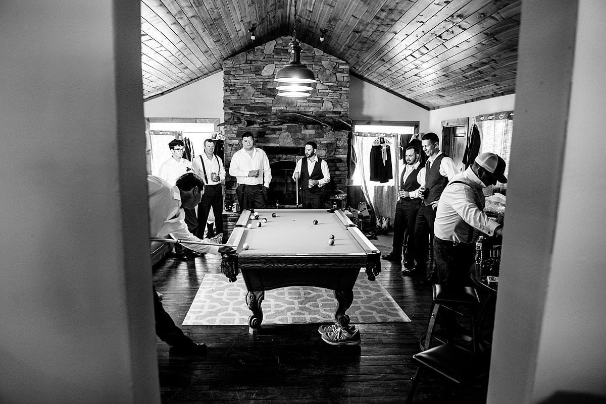 Groomsmen gathered around pooltable playing pool before the ceremony