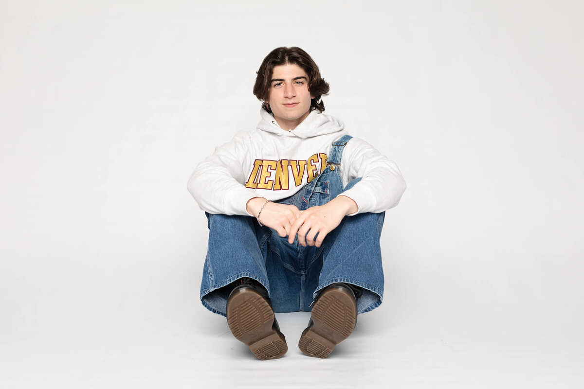 A person with long dark hair sits against a white background, wearing a white hoodie with TENNESSEE on it and blue jeans. They are looking at the camera with a relaxed expression.