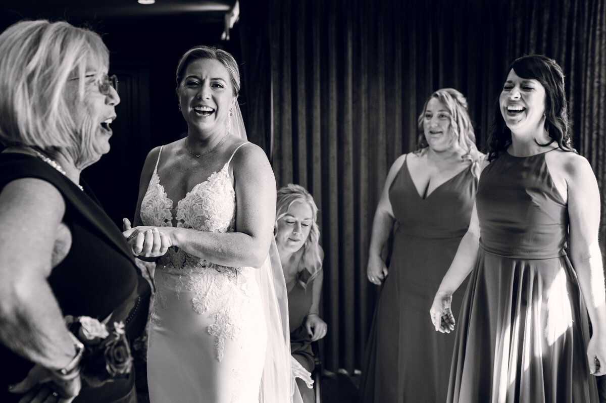 A bride and her bridesmaids laughing in a black and white photo.