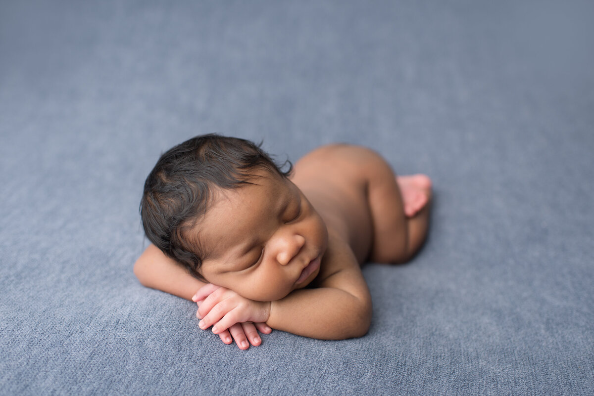 tiny newborn laying on dark blue backdrop