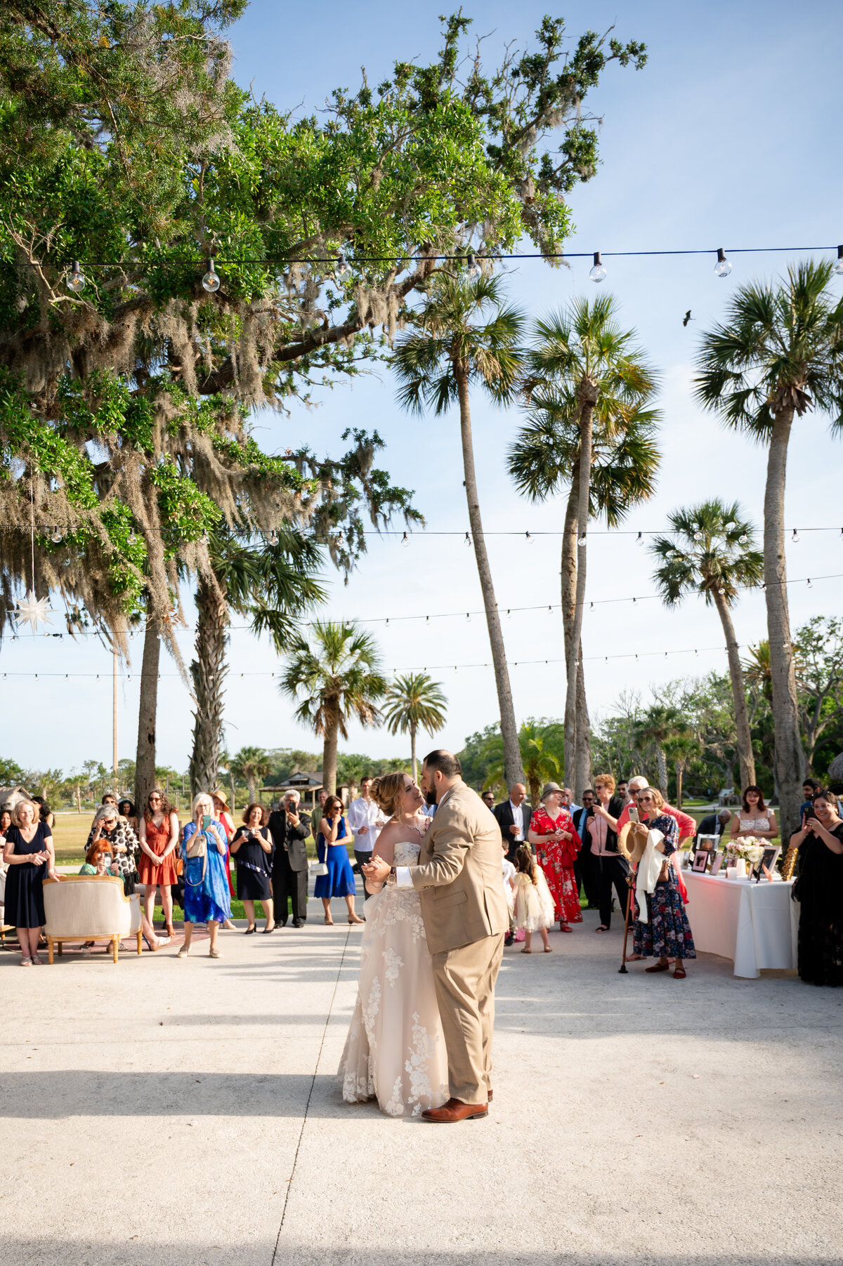 The bride and groom share their first dance under string lights and swaying palm trees during their outdoor wedding reception in St. Augustine, Florida. Surrounded by cheering guests and a lush tropical setting, the couple moves together in a romantic moment as the sun begins to set. Captured by Heartful Films, a Jacksonville wedding photographer and videographer known for documenting candid, joyful wedding moments in naturally beautiful locations.