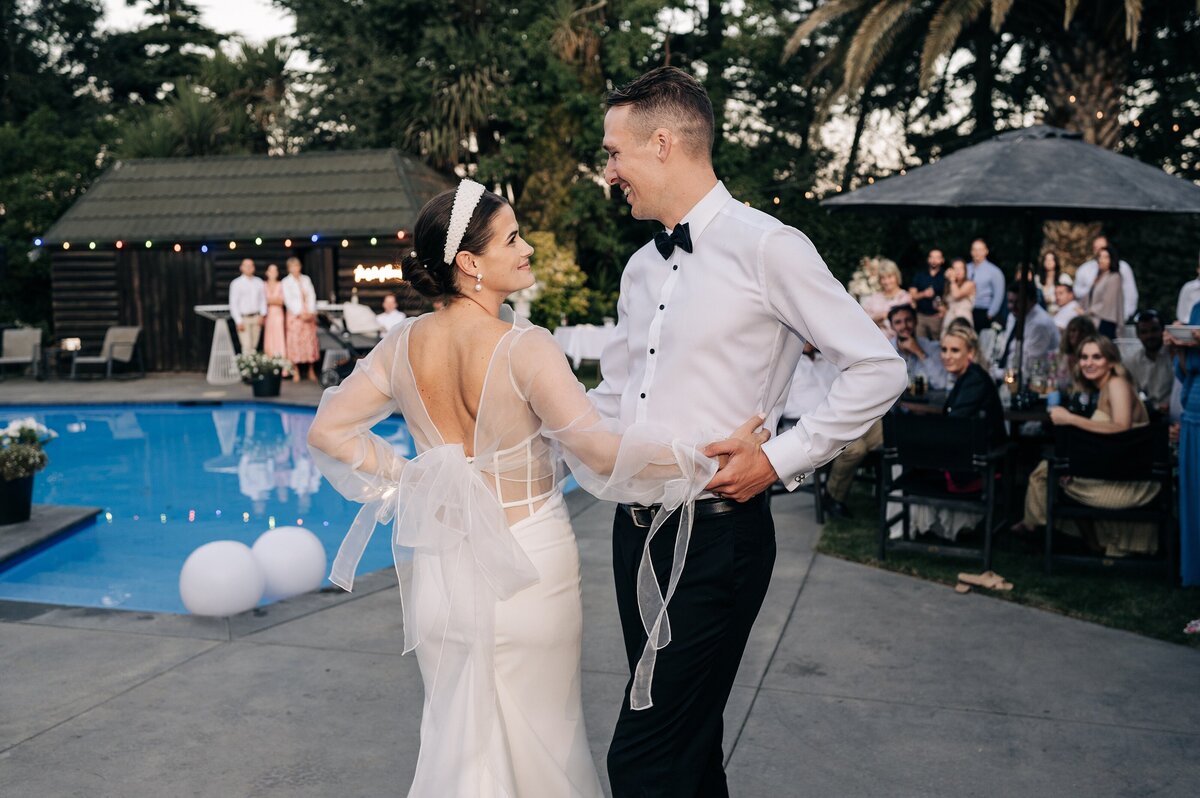 bride and groom have first dance by the pool outdoors in black bowtie and white trish peng dress