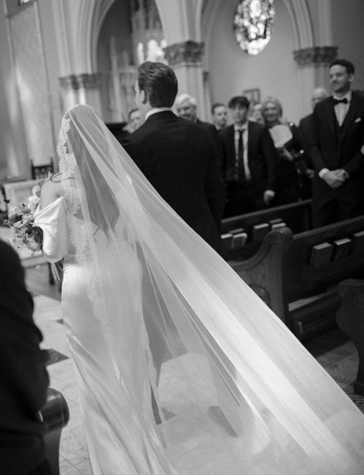 candid wedding photography, black and white, bride's long veil trails down the aisle at St. Paul on the Lake, Michigan