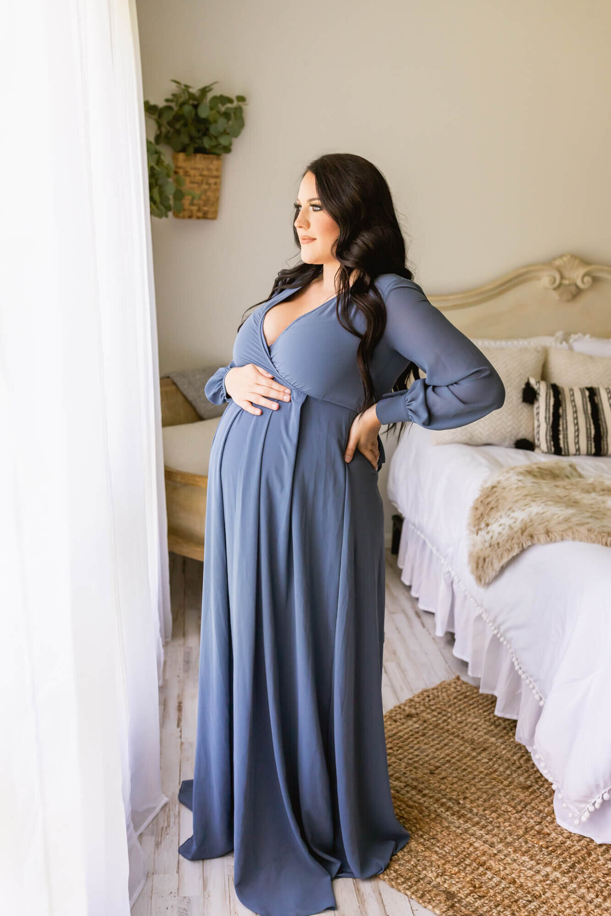 Mother to be in a blue dress looks out the window while caressing her belly