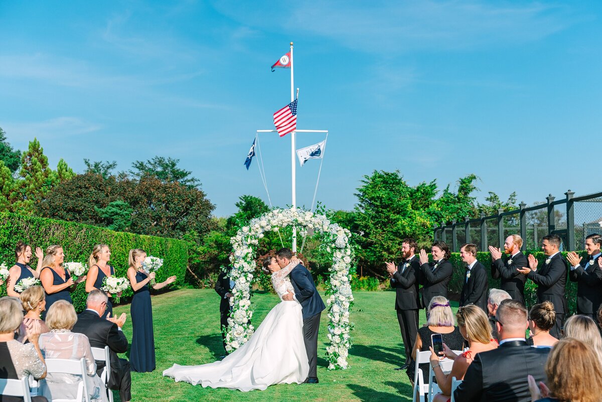 bride and groom share first kiss under a floral arch