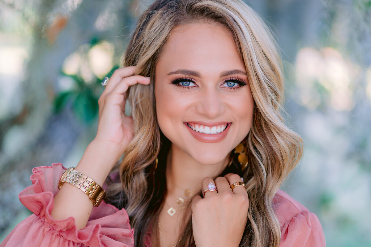 Close-up of smiling senior girl in pink floral top with glowy light and soft Charleston backdrop