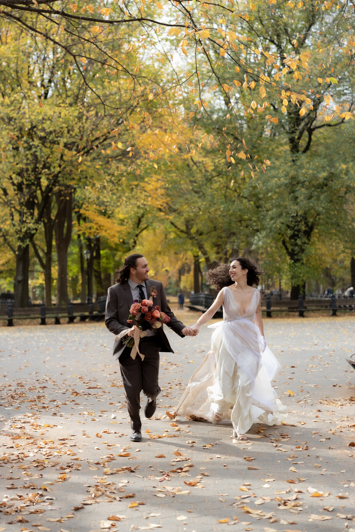 The bride laughing joyfully while holding her bouquet among autumn leaves in Central Park.