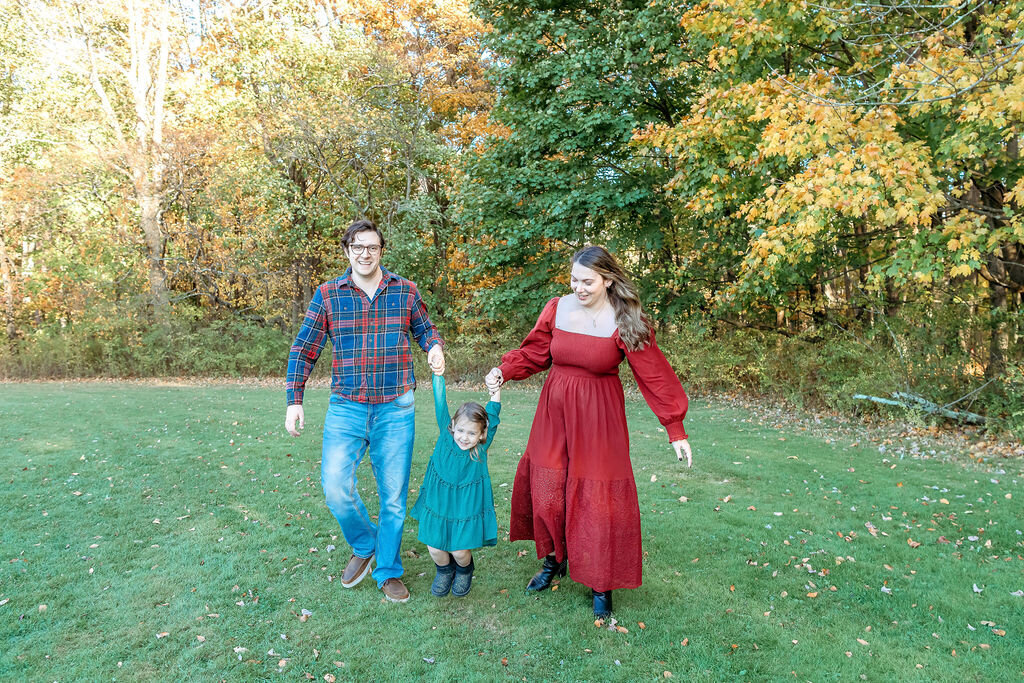 Family of three walking hand in hand through autumn park captured by Connecticut family photographer in natural outdoor setting