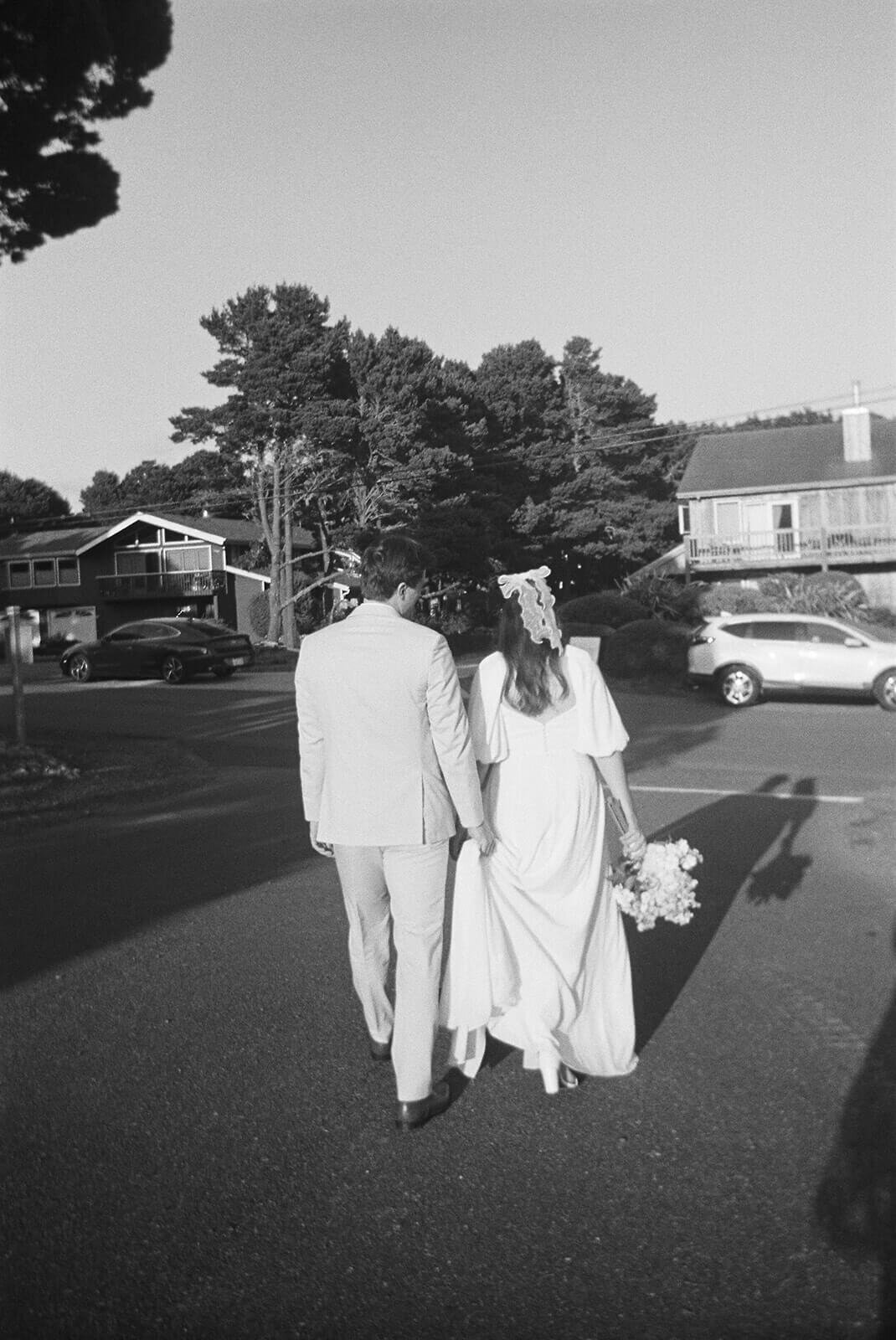 Black and white image of a bride and groom walking away from the camera.