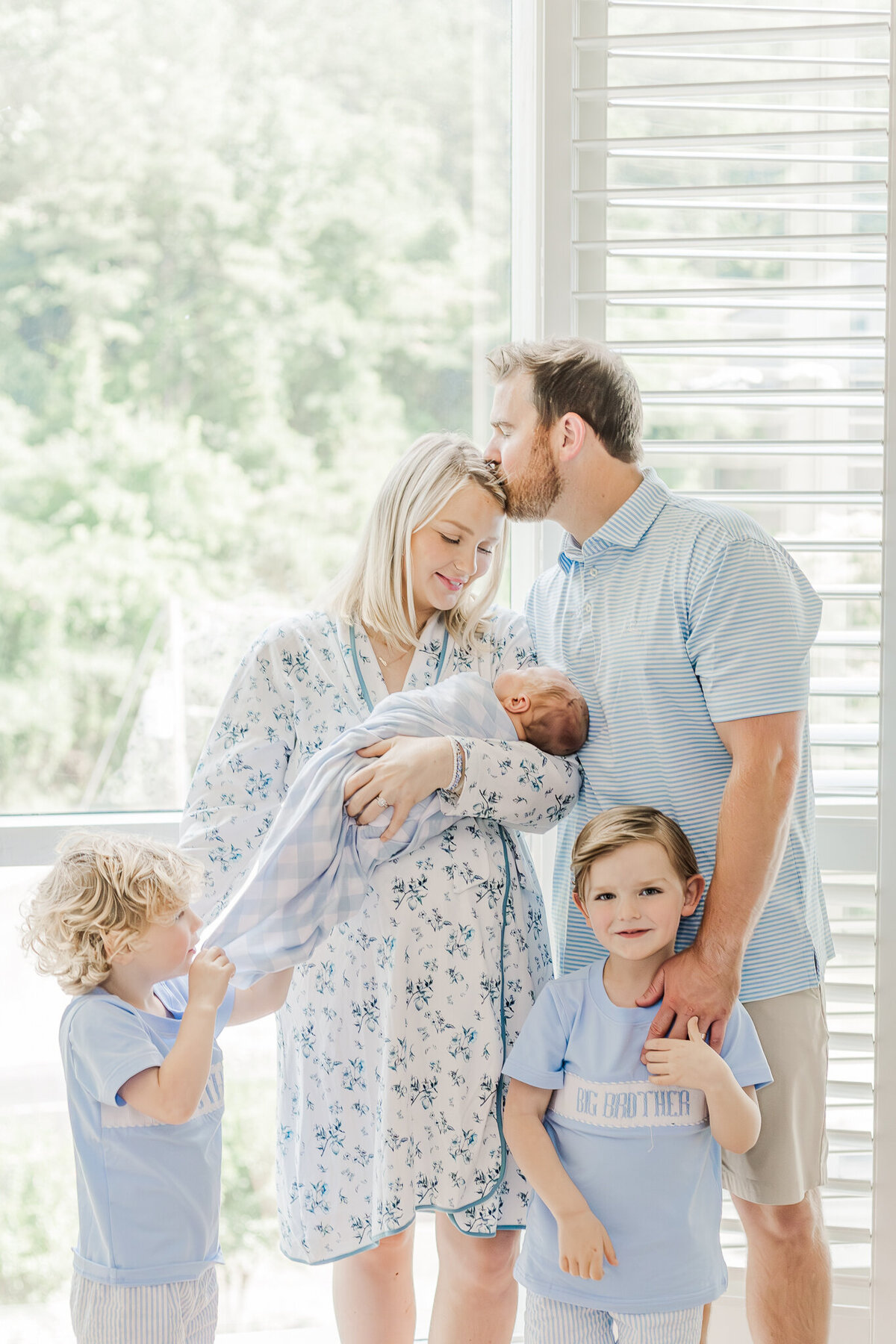 family standing in front of window in hospital during fresh 48 photo session with 5U Photography