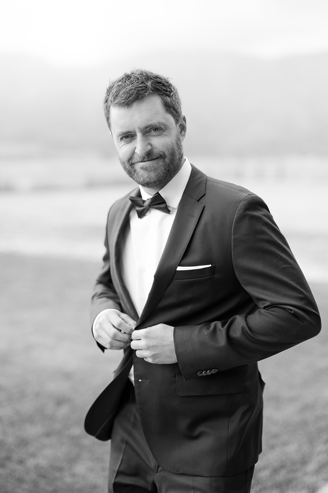 Groom buttons up his suit jacket while walking towards the camera.
