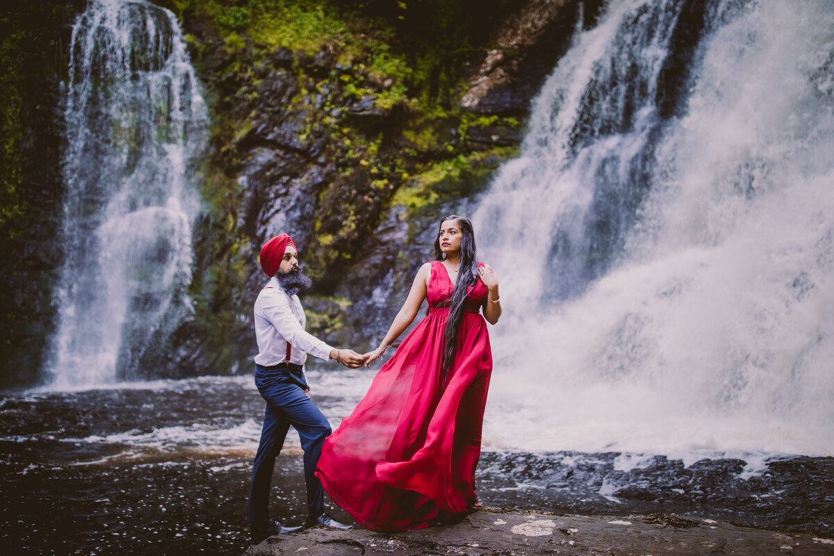 A couple standing in front of two waterfalls called raymondskill falls at the delaware water gap in red outfits