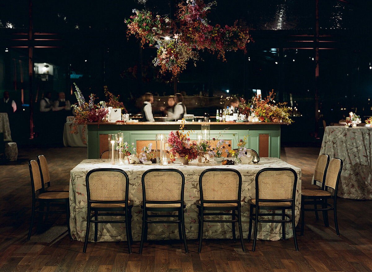Interacting and sculptural floral clouds hang over the dance floor and bars of this fall wedding reception in Tennessee. Clear top tent build out for fall wedding reception in Tennessee hills.  Product clustered floral clouds in a tasteful fall color palette of copper, ruby, gold, burgundy, rust, and lavender. Orchids, bittersweet berries, butterfly ranunculus, and tulips are highlighted. Unique floral design with flower forward large scale installations. Design by Rosemary & Finch Floral Design in Nashville, TN.