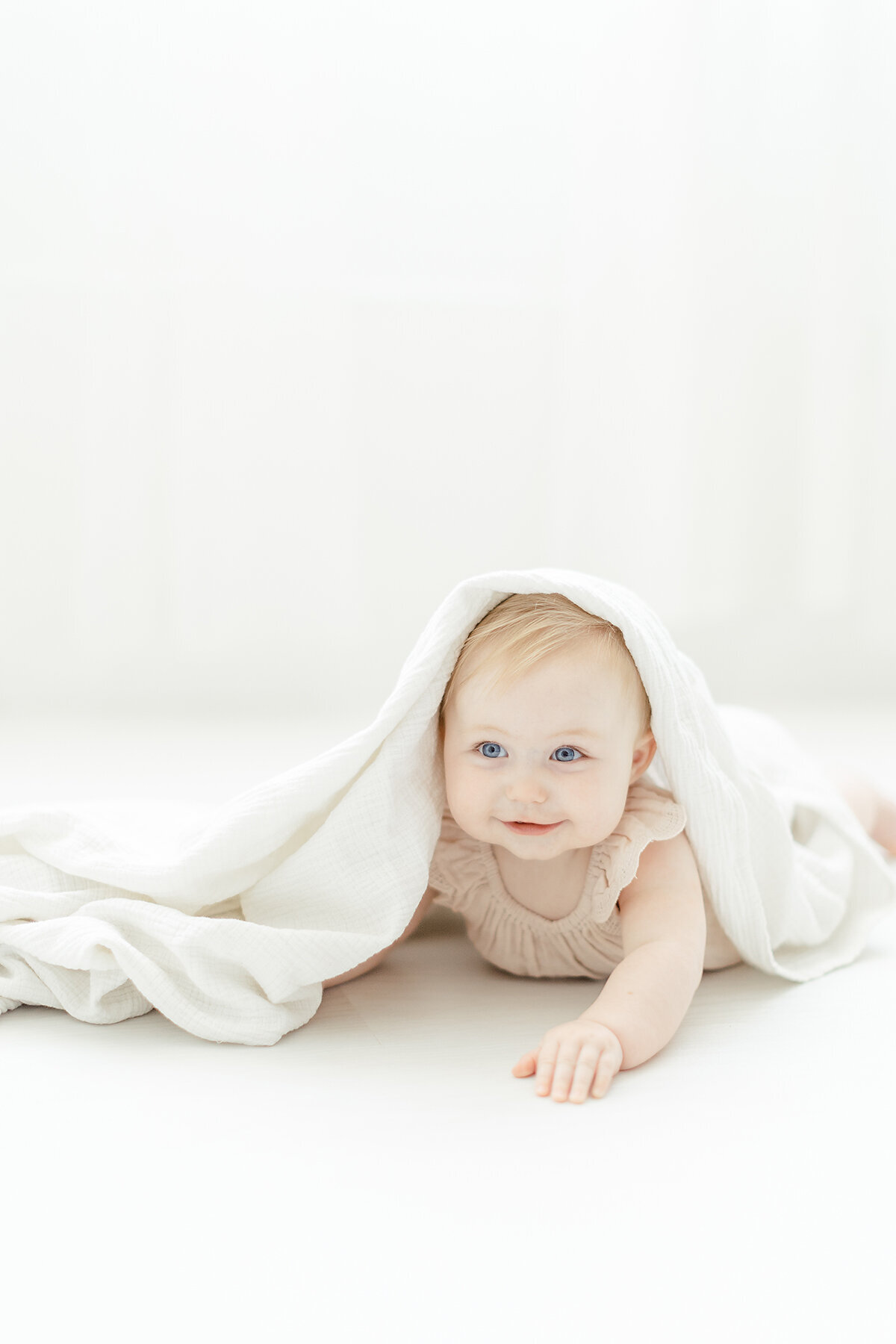 A baby girl playing peek-a-boo on a Dallas photography studio floor for her milestone session.