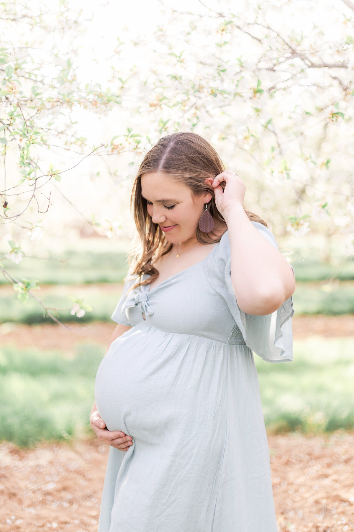 Provo Utah photographer capturing a luxury light and airy photo of a mother posing with a baby bump in this light and airy maternity photo, set in a light and airy orchard in Utah.