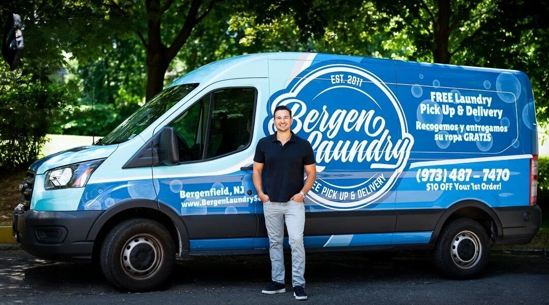 Professional headshot of man in casual outfit standing confidently outdoors beside branded company van new jersey.