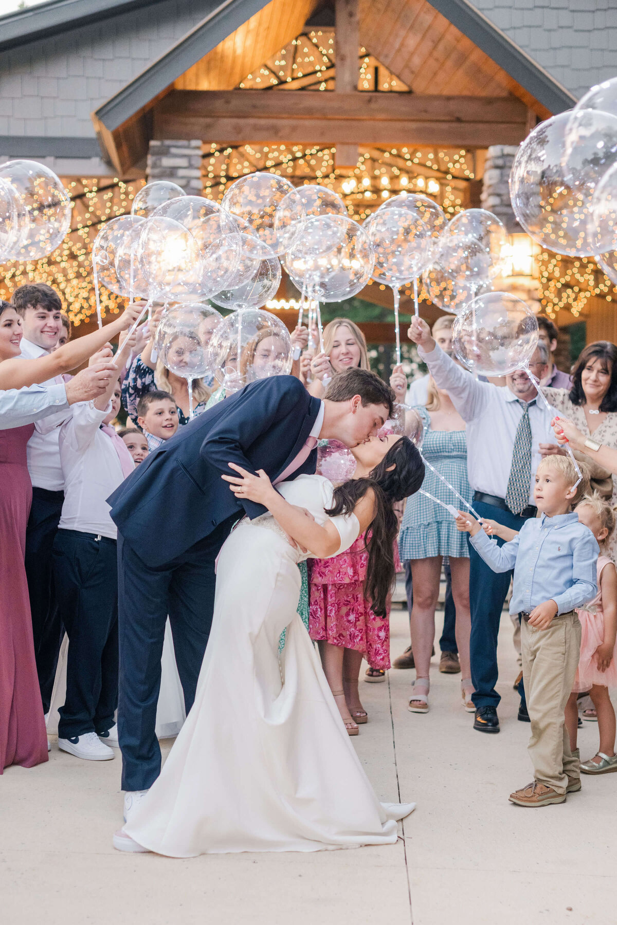 Bride and groom kissing for wedding exit surrounded by balloons
