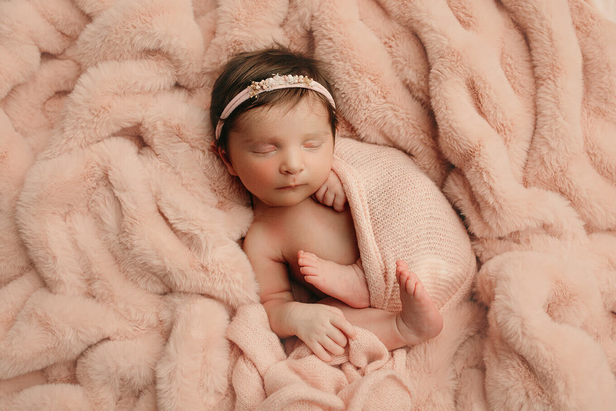 photo of newborn girl with lots of hair sleeping on her back wrapped in pink