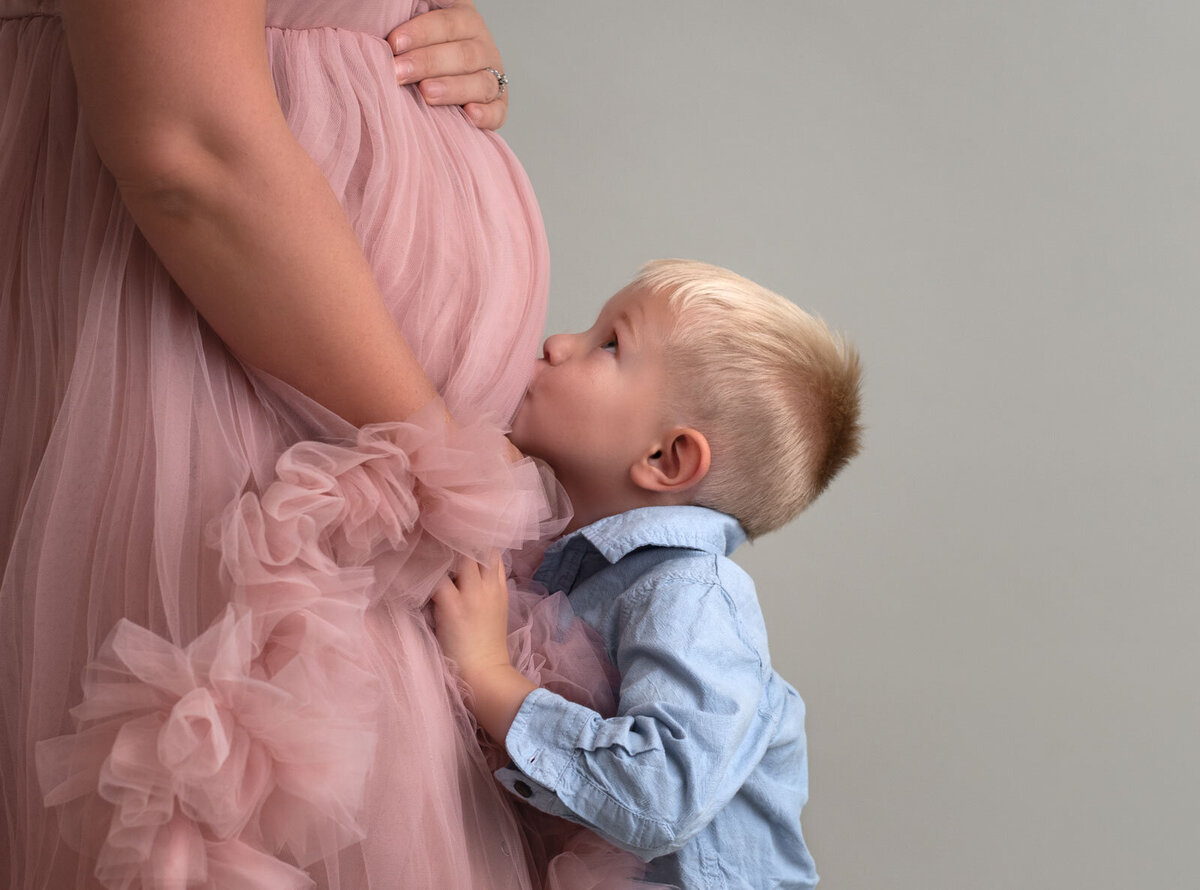boy kissing mom's belly at maternity photoshoot