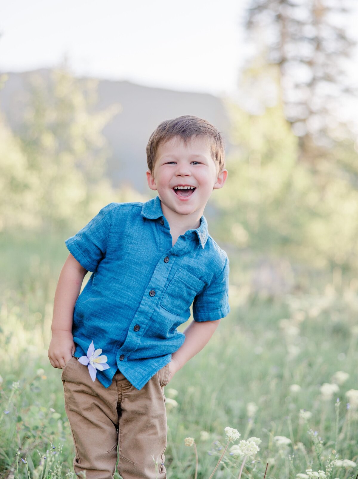 A laughing toddler boy in a blue shirt plays in a wildflowers field in summer