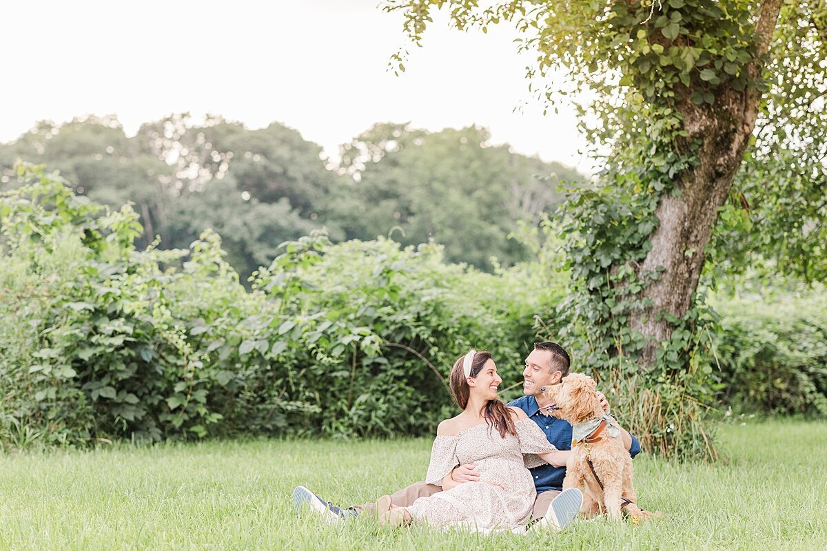 couples sits with dog during maternity photo session with Sara Sniderman Photography at Heard Farm in Wayland Massachusetts