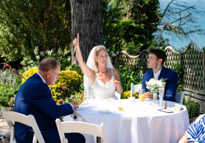 A bride and groom sitting at a table with their arms in the air