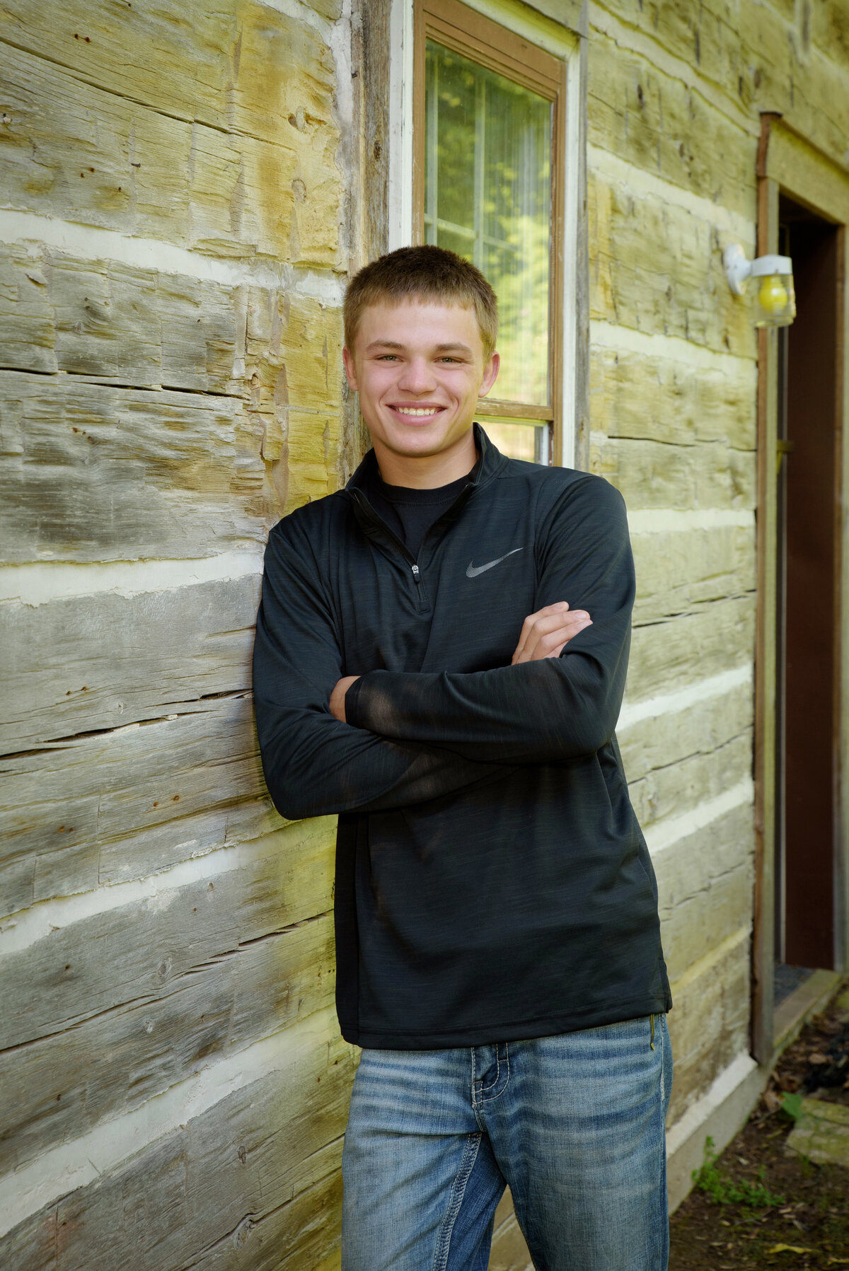 Luxemburg Casco high school senior boy wearing a long sleeve black shirt and jeans leaning against barn wood wall at Devil's River Campground near Green Bay, Wisconsin