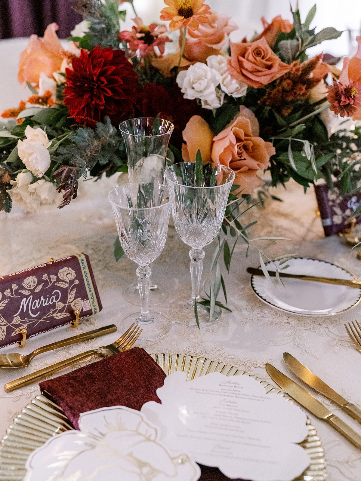 Romantic reception table with crystal glassware, custom chocolate place cards, and lush florals—elevated vineyard elegance with personal charm.