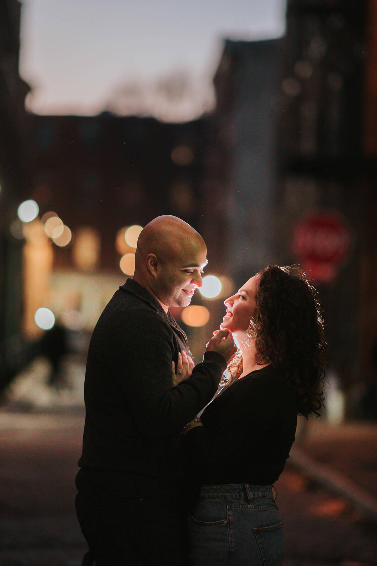 A couple shares an intimate moment on a dimly lit city street at night, illuminated by soft, romantic lighting