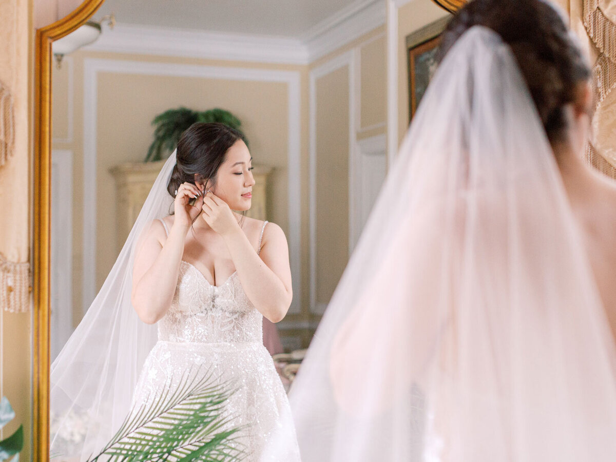 Bride puts on earrings in front of a mirror