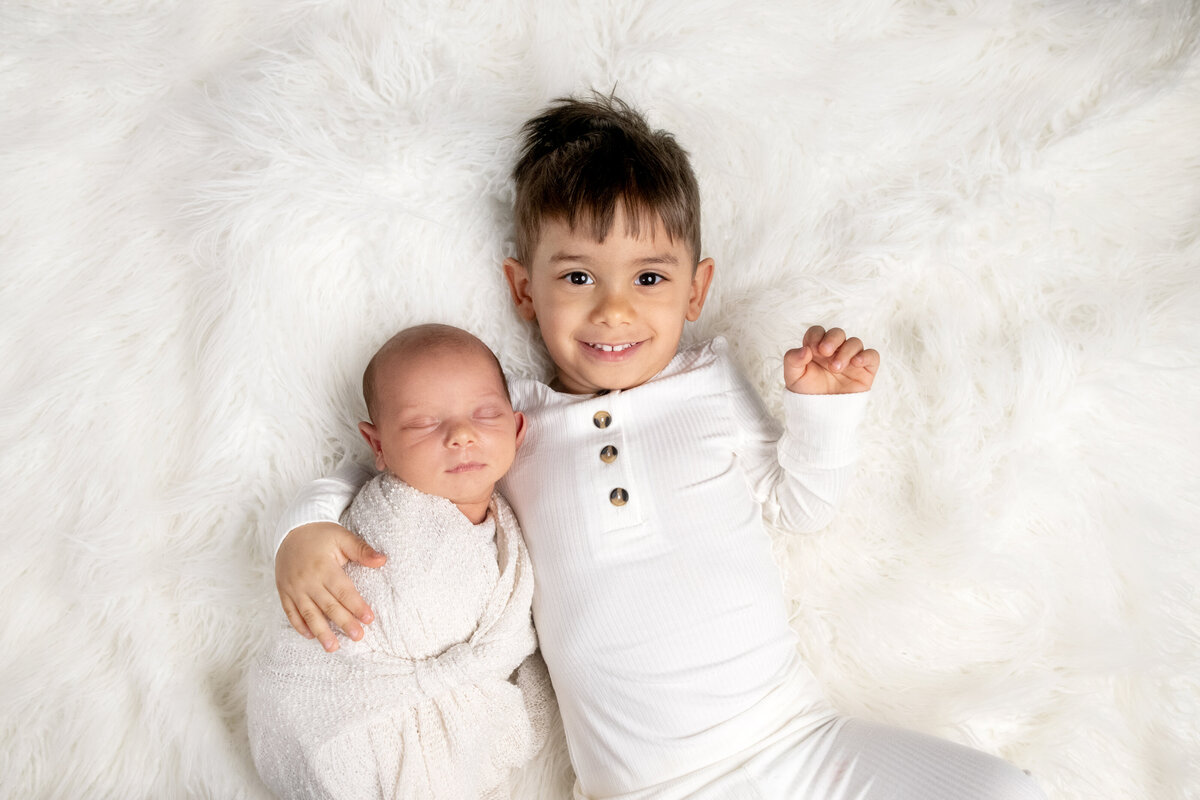 Smiling big brother laying on white fuzzy rug with baby brother