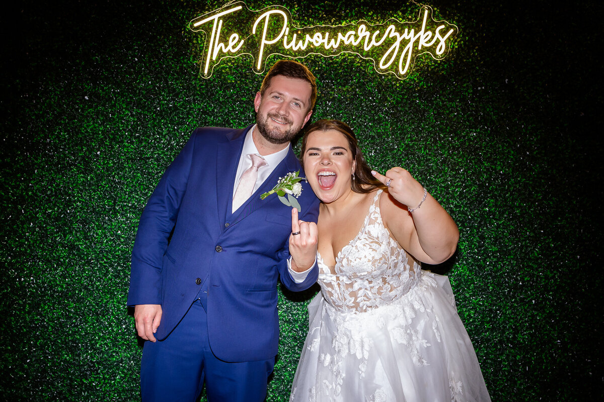 bride and groom showing off wedding bands in front of ivy wall with neon sign by NH Wedding Photographer Lisa Smith Photography