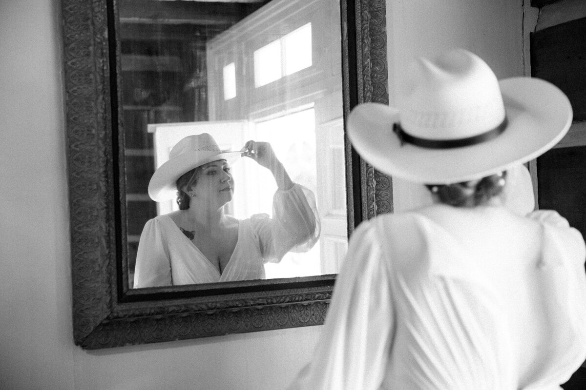 Bride adjusts her cowboy had in a mirror following her elopement ceremony in Tennessee. 