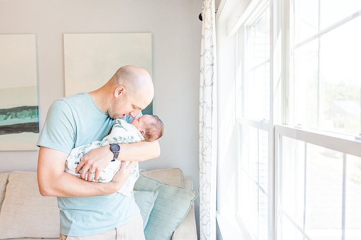 dad holds baby near window dung in-home newborn photo session with Sara Sniderman Photography in metro west Boston  Massachusetts