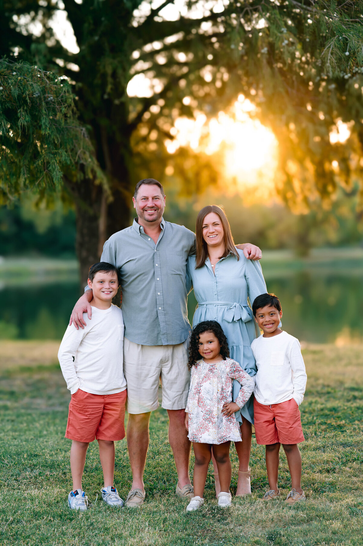 Parents and children standing together in a sunlit field during a family photography session in Frisco, Texas. Natural, timeless portrait by Jennifer L. Kirk Photography.