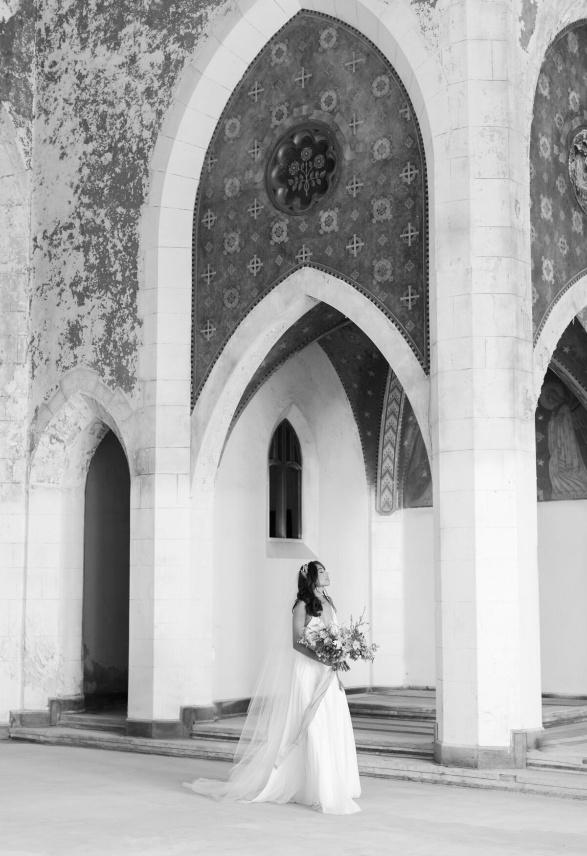 peaceful bride under crumbling arches of abandoned cathedral, ruins wedding venue in Europe