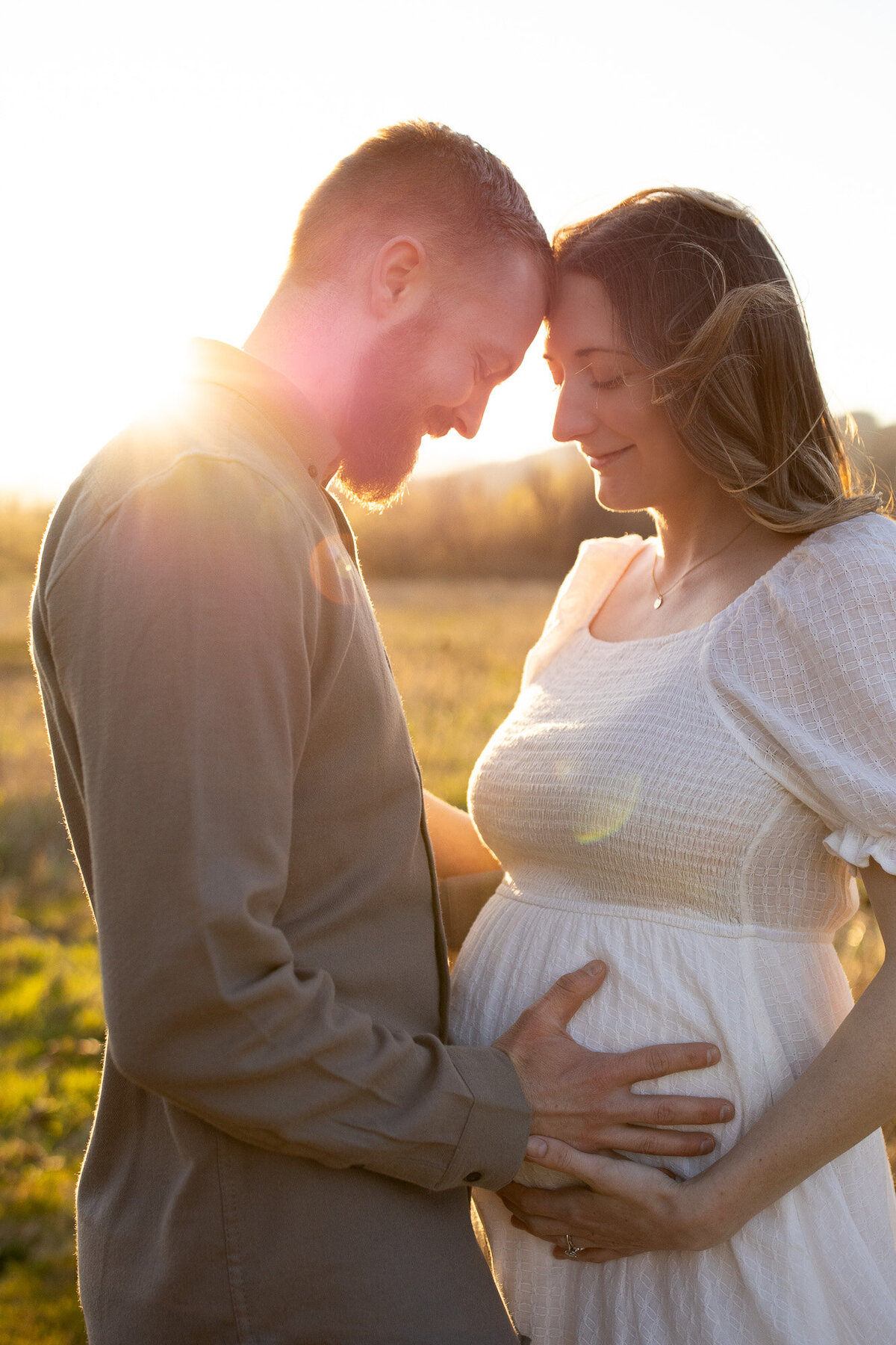 Couple holding woman's pregnant belly at sunset in a field.