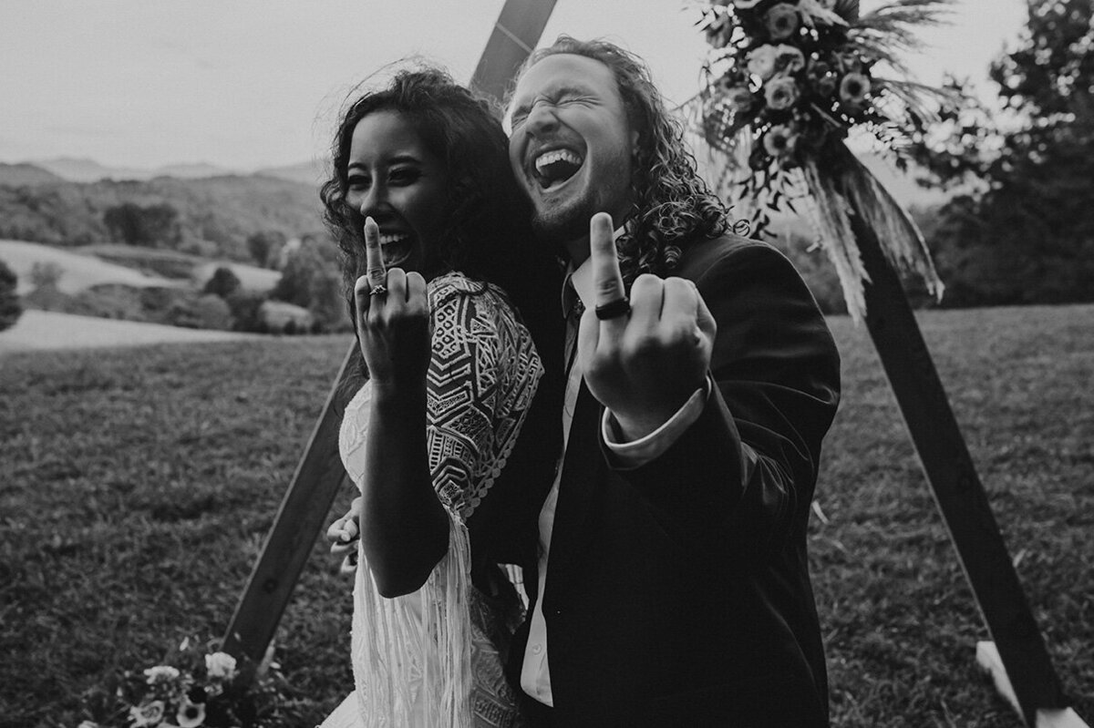 bride and groom pose holding up ring finger displaying wedding bands in the outdoors