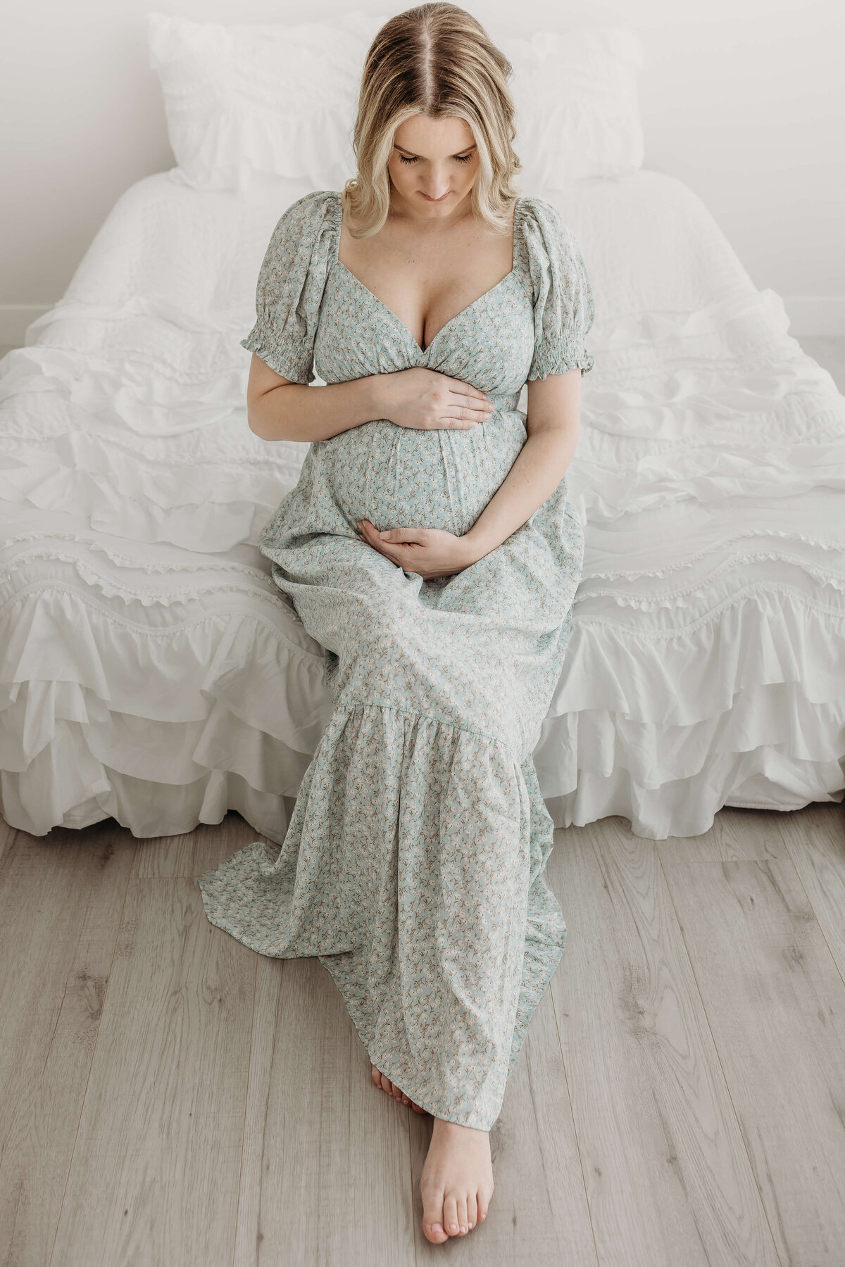 Pregnant mom in blue and green dress sitting on bed